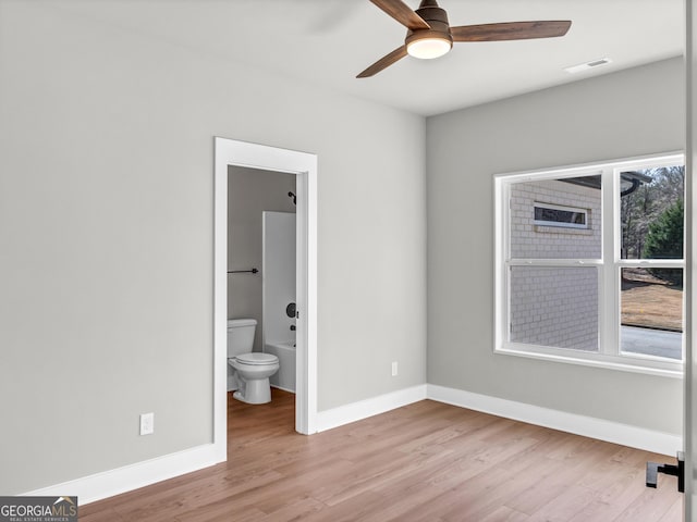 unfurnished bedroom with ensuite bath, visible vents, wood finished floors, and baseboards