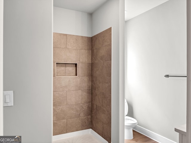 bathroom featuring baseboards, toilet, wood finished floors, and a tile shower