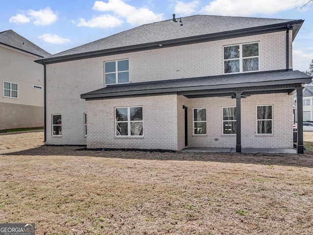 rear view of house with brick siding, a lawn, and a patio