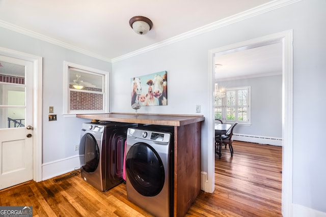 clothes washing area featuring hardwood / wood-style flooring, ornamental molding, baseboard heating, and washing machine and clothes dryer