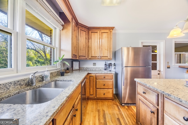 kitchen with light stone countertops, a sink, appliances with stainless steel finishes, crown molding, and light wood-type flooring