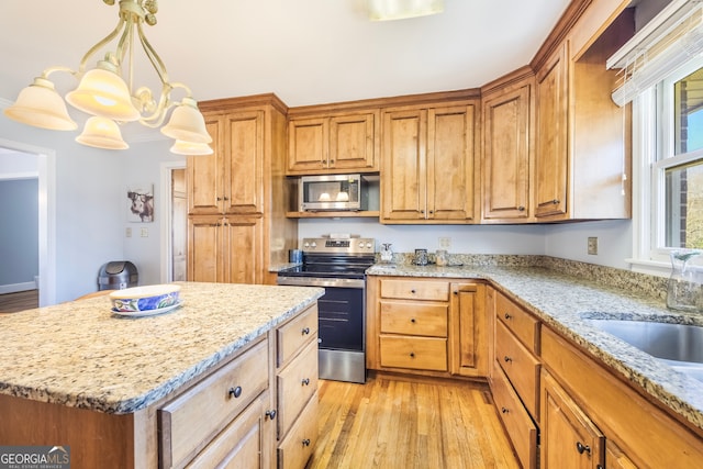 kitchen featuring decorative light fixtures, light wood-style flooring, stainless steel appliances, and light stone countertops