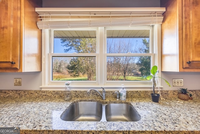 kitchen featuring a sink, brown cabinets, and light stone counters