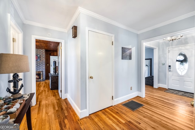 foyer featuring visible vents, a brick fireplace, crown molding, and light wood-style floors