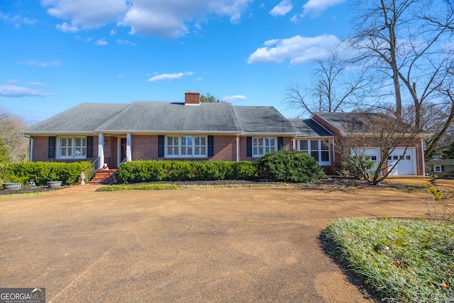 ranch-style house featuring driveway, brick siding, a chimney, and an attached garage