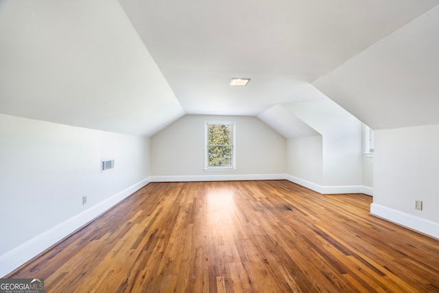 additional living space with visible vents, wood-type flooring, baseboards, and vaulted ceiling