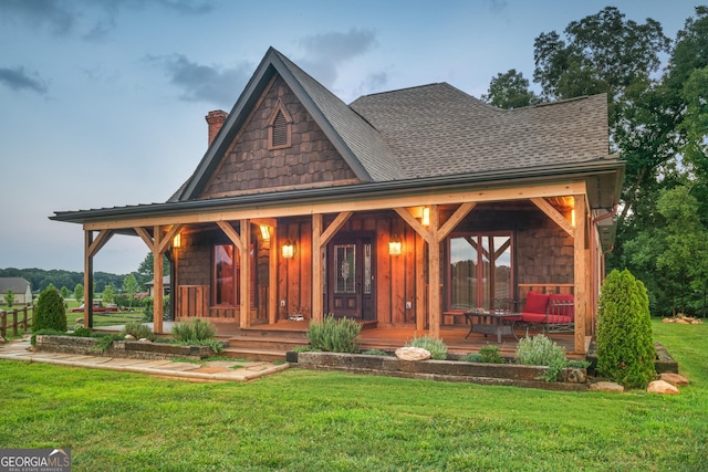 view of front of home featuring a chimney, roof with shingles, a porch, and a front yard