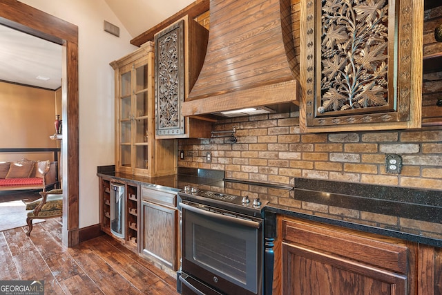 kitchen featuring dark wood-type flooring, custom range hood, glass insert cabinets, stainless steel range with electric cooktop, and decorative backsplash