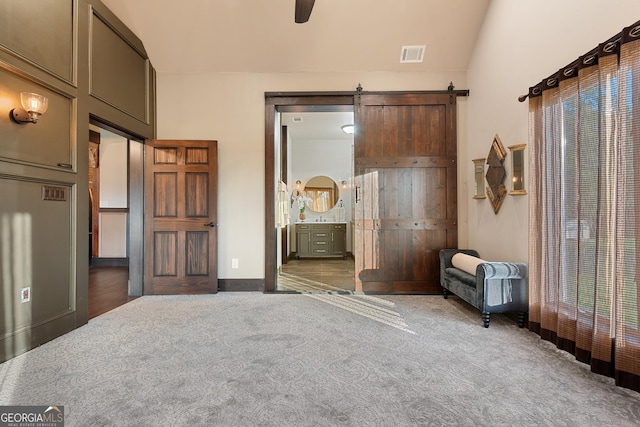 carpeted bedroom featuring visible vents, ensuite bath, lofted ceiling, and a barn door