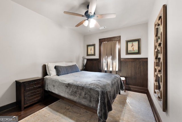 bedroom with wooden walls, wood finished floors, a wainscoted wall, visible vents, and ceiling fan