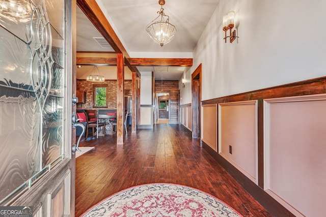 entrance foyer featuring visible vents, beam ceiling, a wainscoted wall, hardwood / wood-style flooring, and a chandelier