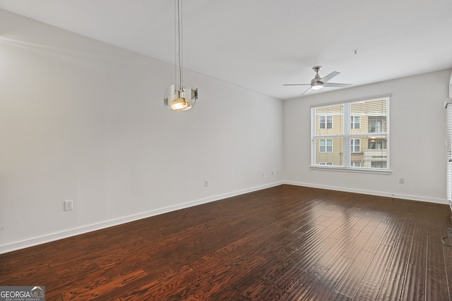 empty room featuring baseboards, dark wood-style floors, and a ceiling fan