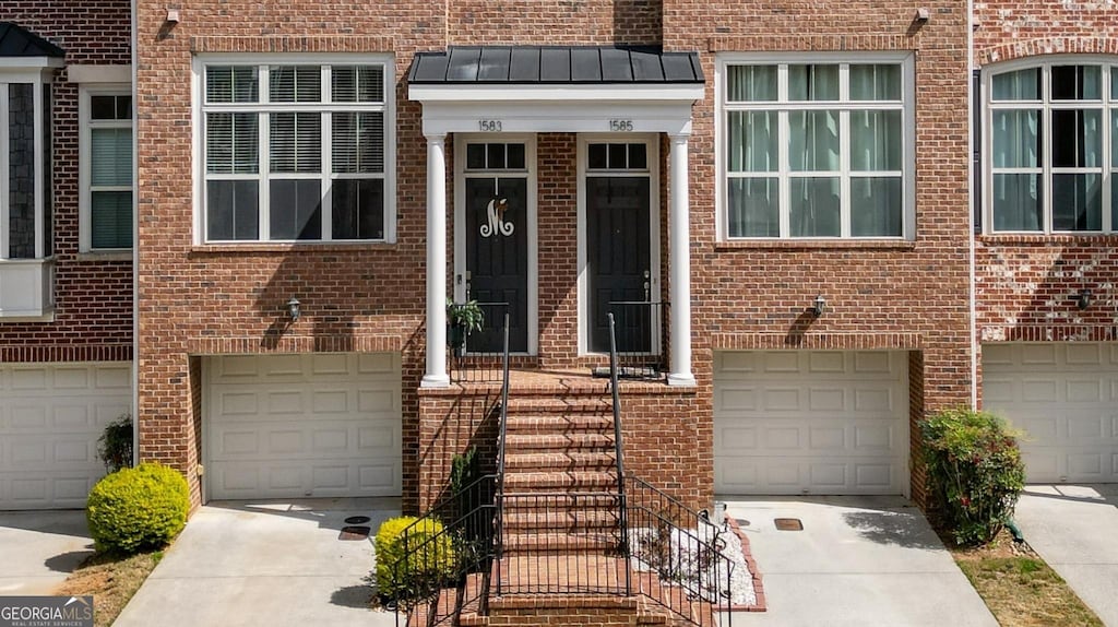 doorway to property featuring brick siding, an attached garage, metal roof, and a standing seam roof