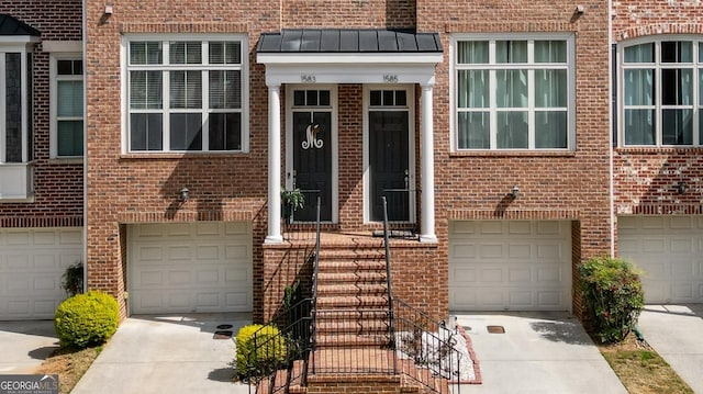 doorway to property featuring brick siding, an attached garage, metal roof, and a standing seam roof