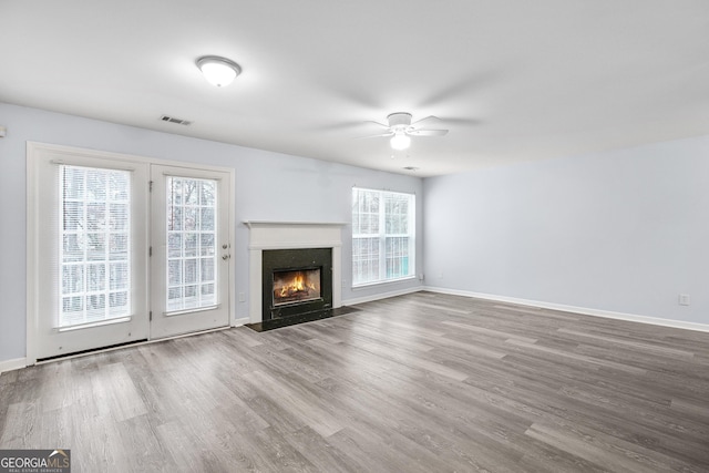 unfurnished living room featuring visible vents, baseboards, a fireplace with flush hearth, wood finished floors, and a ceiling fan