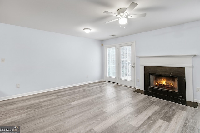 unfurnished living room with a ceiling fan, visible vents, wood finished floors, baseboards, and a fireplace with flush hearth