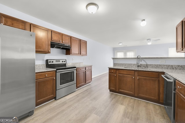 kitchen with a sink, under cabinet range hood, stainless steel appliances, light wood-style floors, and a peninsula