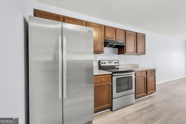 kitchen with light stone countertops, brown cabinetry, light wood finished floors, stainless steel appliances, and under cabinet range hood