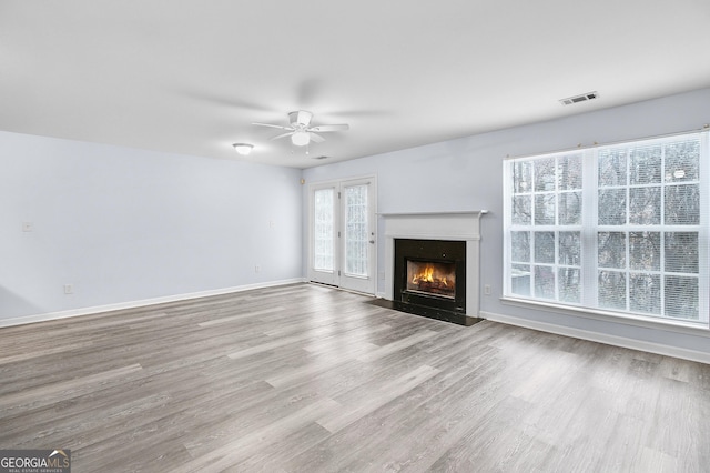 unfurnished living room featuring visible vents, ceiling fan, baseboards, a fireplace with flush hearth, and wood finished floors