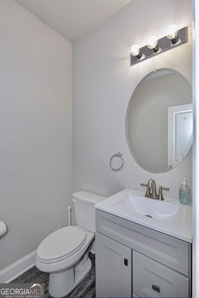 bathroom with baseboards, toilet, wood finished floors, and vanity