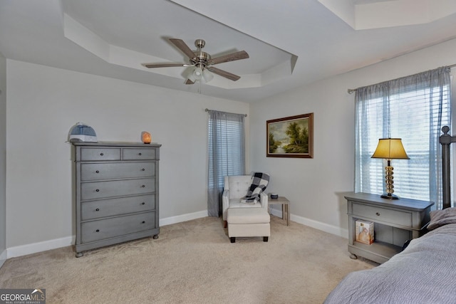 bedroom with a raised ceiling, light colored carpet, baseboards, and ceiling fan