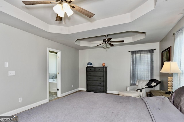 carpeted bedroom with a raised ceiling, connected bathroom, baseboards, and ceiling fan