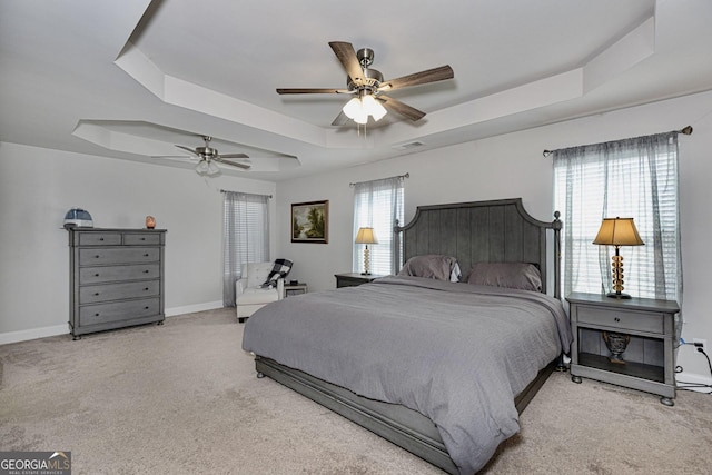 carpeted bedroom with a ceiling fan, a tray ceiling, baseboards, and visible vents