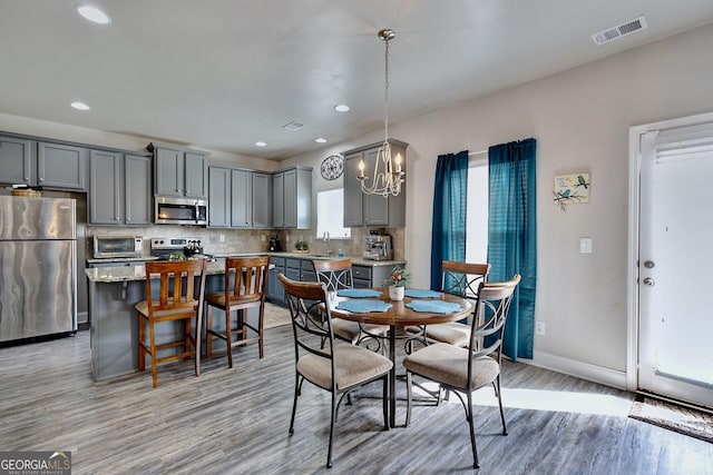 dining area with light wood finished floors, visible vents, baseboards, a chandelier, and a toaster