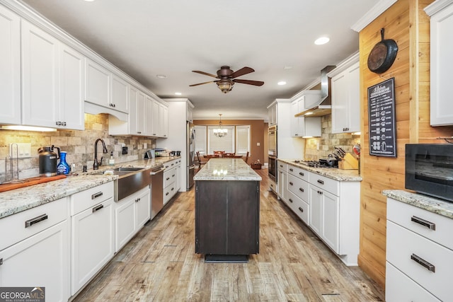 kitchen featuring a sink, white cabinetry, appliances with stainless steel finishes, wall chimney exhaust hood, and light wood finished floors