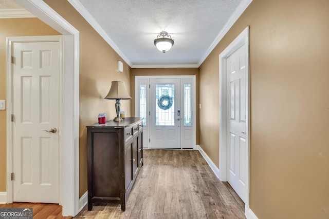 foyer with ornamental molding, a textured ceiling, baseboards, and wood finished floors