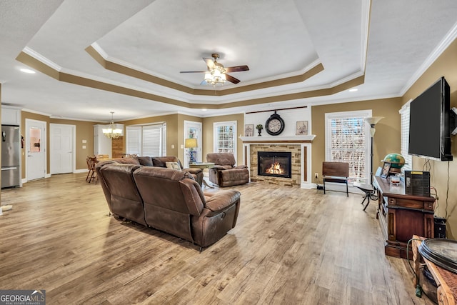 living area with a glass covered fireplace, a tray ceiling, light wood-type flooring, and a wealth of natural light