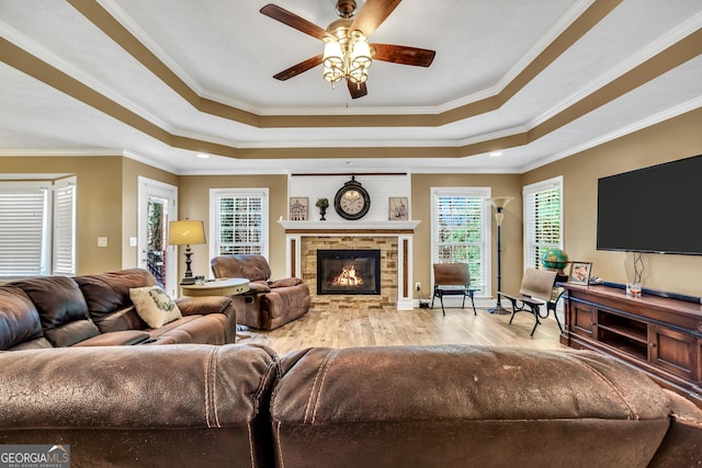 living area with a stone fireplace, a tray ceiling, wood finished floors, and ornamental molding