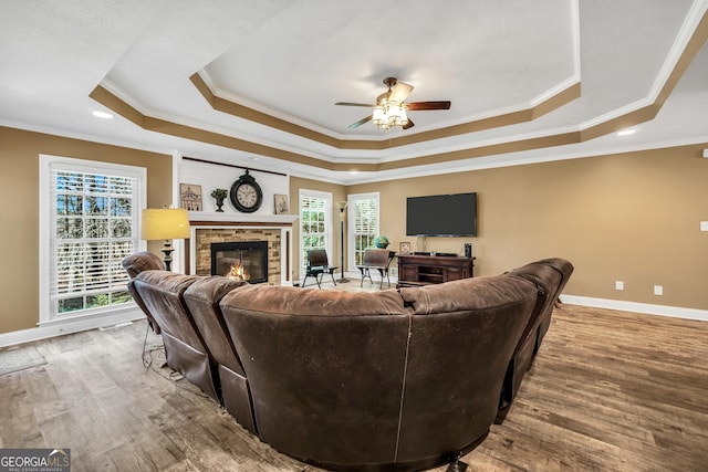 living room featuring a tray ceiling, baseboards, wood finished floors, and a fireplace