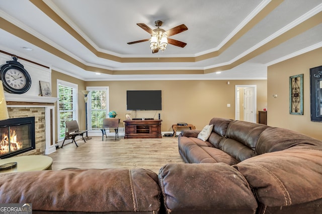 living area with ornamental molding, a fireplace, a raised ceiling, and wood finished floors