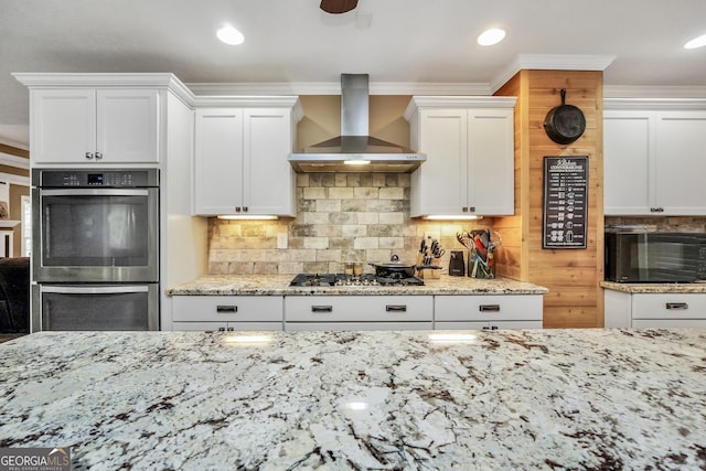 kitchen with light stone counters, stainless steel appliances, white cabinetry, wall chimney exhaust hood, and tasteful backsplash