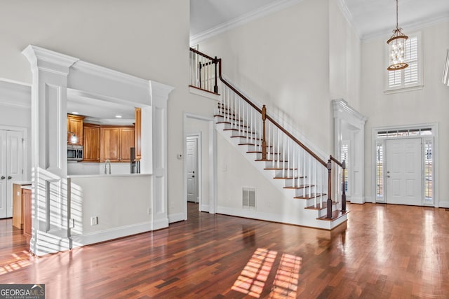 entrance foyer with wood finished floors, baseboards, visible vents, ornamental molding, and stairs
