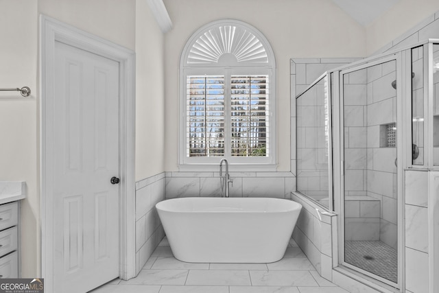 full bathroom featuring lofted ceiling, a stall shower, a freestanding tub, marble finish floor, and vanity