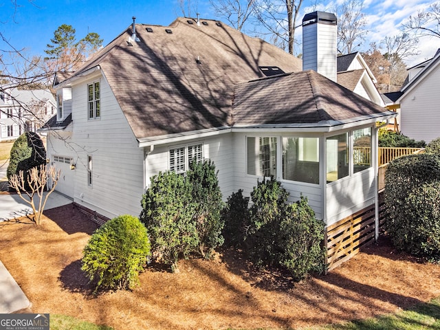 view of property exterior featuring a garage, roof with shingles, a chimney, and driveway