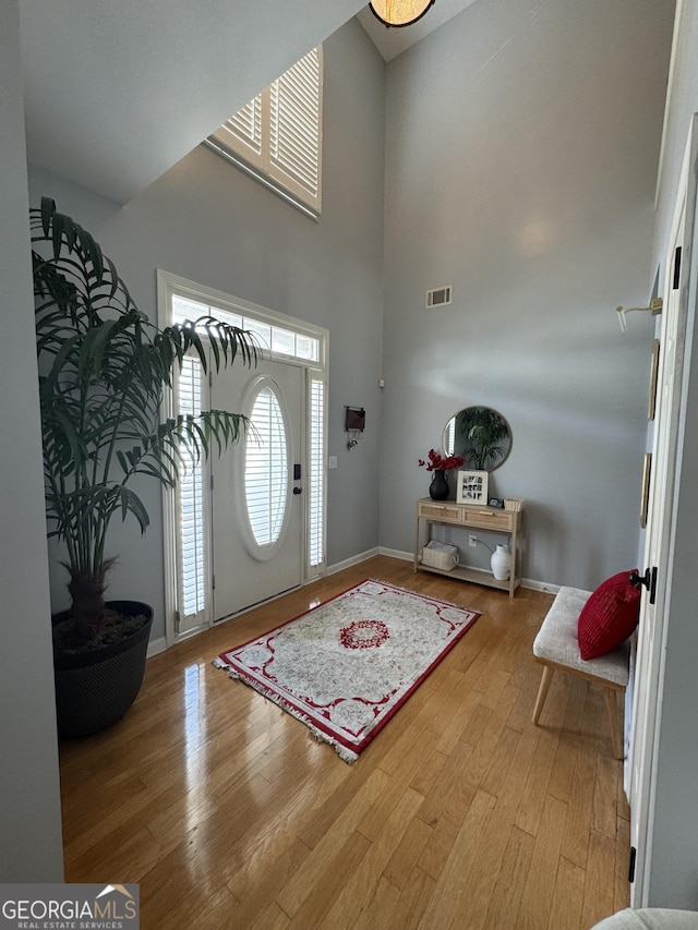 entryway with visible vents, wood finished floors, baseboards, and a towering ceiling