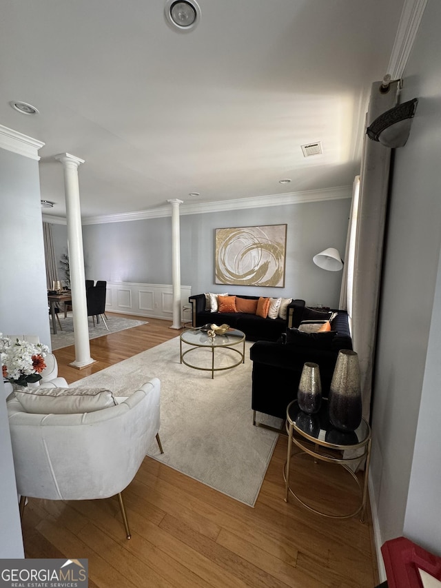 living area featuring wood finished floors, visible vents, decorative columns, wainscoting, and crown molding