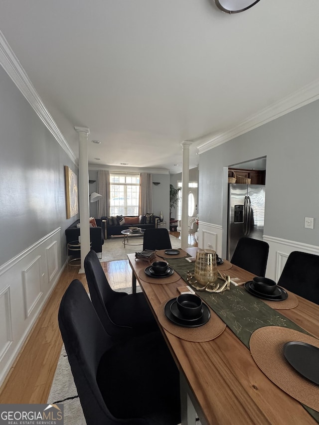 dining area featuring crown molding, decorative columns, light wood-style floors, and wainscoting