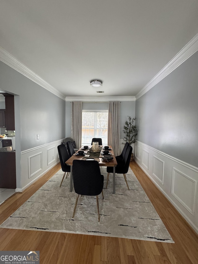 dining area with ornamental molding, wood finished floors, and wainscoting