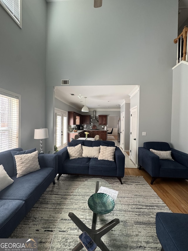 living area with light wood finished floors, visible vents, a towering ceiling, and ornamental molding