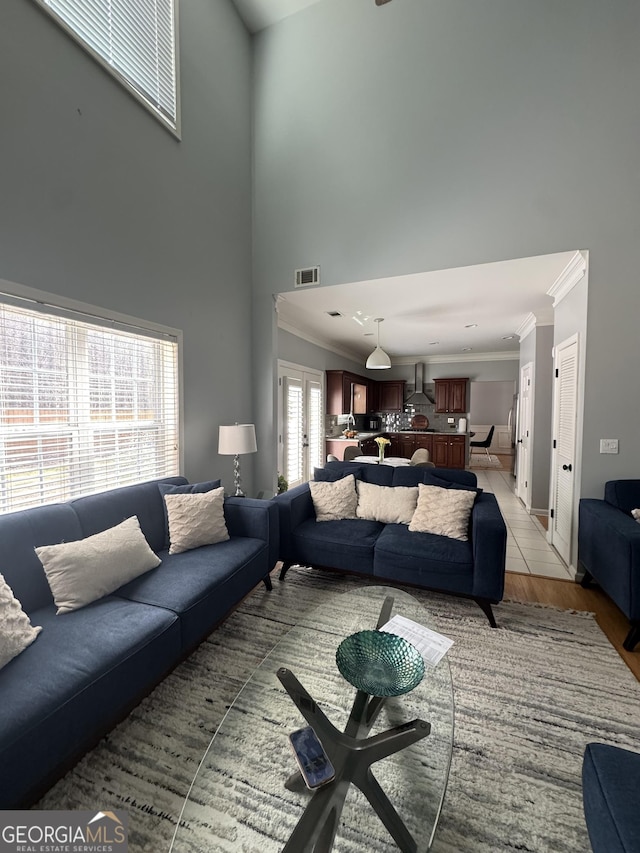 living room with crown molding, light wood-style flooring, visible vents, and a towering ceiling