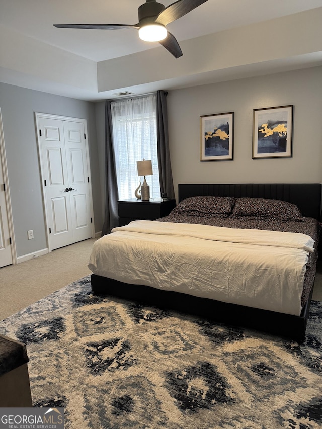 bedroom with visible vents, baseboards, ceiling fan, a tray ceiling, and carpet flooring