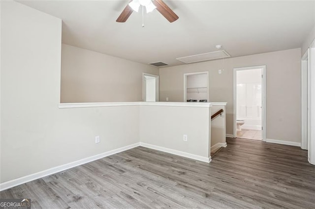 spare room with visible vents, baseboards, attic access, wood finished floors, and a ceiling fan