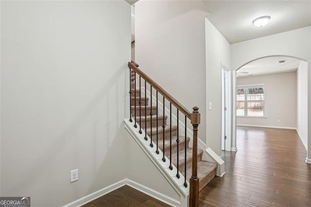 stairway with wood finished floors, arched walkways, and baseboards