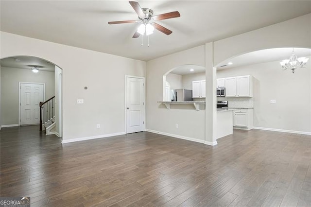 unfurnished living room featuring dark wood-style floors, ceiling fan with notable chandelier, and baseboards