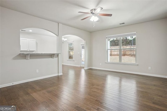 unfurnished living room featuring visible vents, ceiling fan with notable chandelier, dark wood-style floors, arched walkways, and baseboards