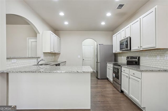 kitchen featuring light stone counters, visible vents, arched walkways, a sink, and appliances with stainless steel finishes